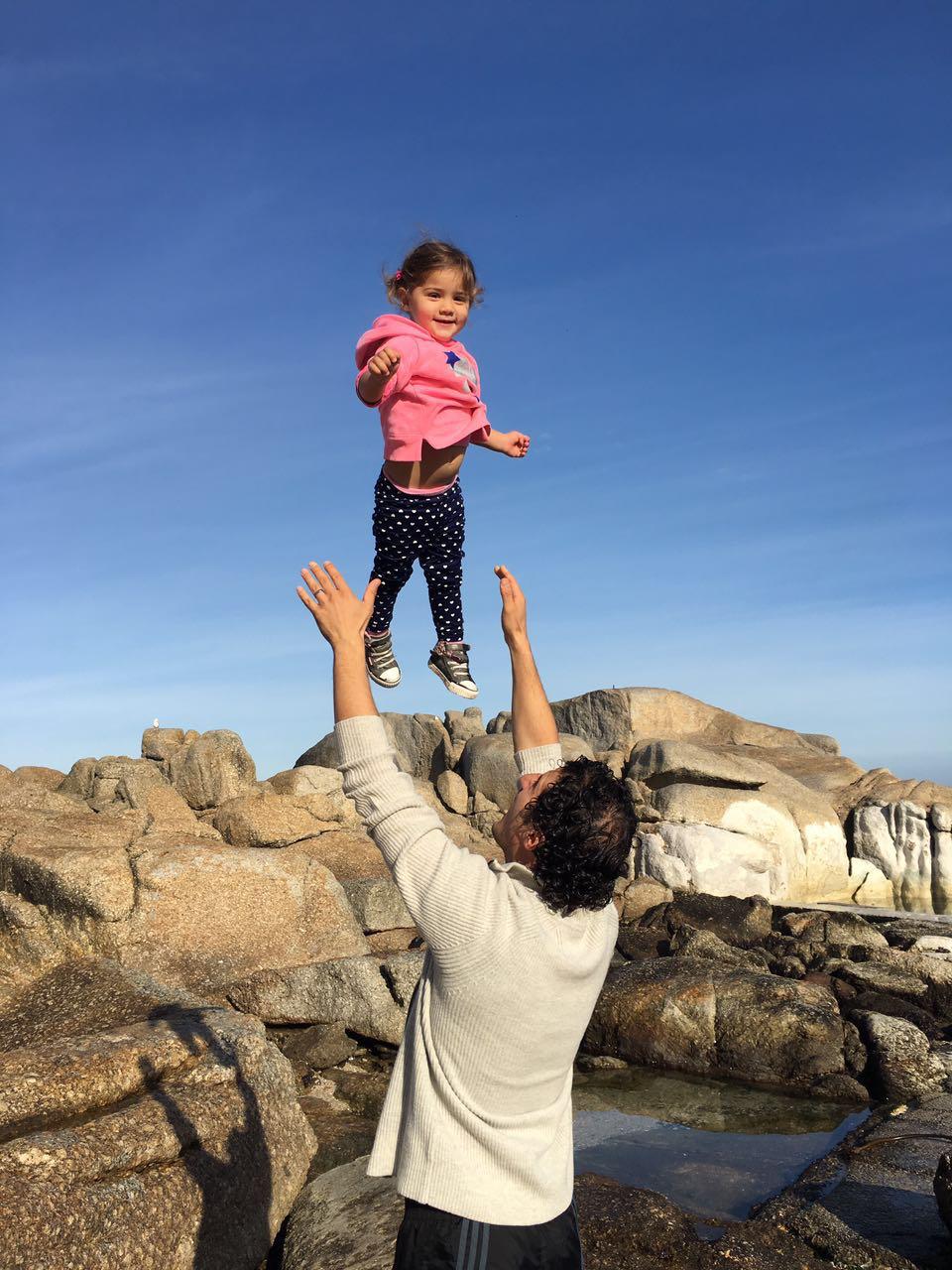 Mica flying through the air with Dad on the rocks