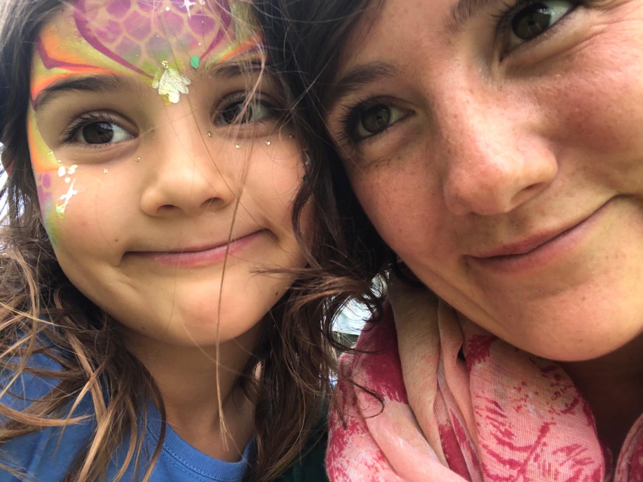 Mica in mermaid face paint cheek-to-cheek with Mom